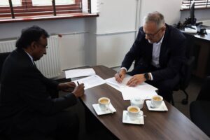 Rektor PANS w Głogowie, dr Jarosław Hermaszewski oraz Prezes American Medical Academy – John K. Eapen. Panowie w garniturach, w gabinecie, przy stole podpisują list intencyjny o współpracy pomiędzy instytucjami.