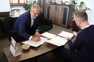 Rektor PANS w Głogowie: dr Jarosław Hermaszewski i przedstawiciel Pulse of Mind: Mindaugas Latisenka podpisują porozumienie współpracy, przy stole, w Biurze Rektora.