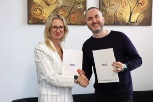 Mgr Anna Akielaszek-Witczak – Uczelniany Koordynator Programu Erasmus+.i przedstawiciel Pulse of Mind: Mindaugas Latisenka podają sobie dłonie w Biurze Rektora. W drugich dłoniach trzymają teczki z dokumentami.