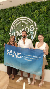 Uczelniany Koordynator Programu Erasmus+ PANS w Głogowie i instytucji partnerskiej pozują do zdjęcia z flagą uczelni podczas mobilności Erasmus+ w Maladze.